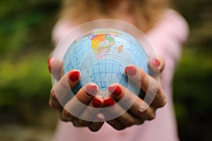 The girl in a pink sweater with red manicure holds a small globe with geografical names in Ukrainian cyrillic letters on