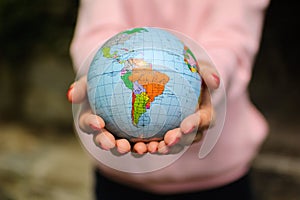 The girl in a pink sweater with red manicure holds a small globe with geografical names in Ukrainian cyrillic letters on
