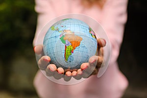 The girl in a pink sweater with red manicure holds a small globe with geografical names in Ukrainian cyrillic letters on