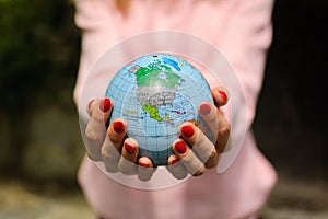 The girl in a pink sweater with red manicure holds a small globe with geografical names in Ukrainian cyrillic letters on