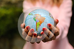 The girl in a pink sweater with red manicure holds a small globe with geografical names in Ukrainian cyrillic letters on