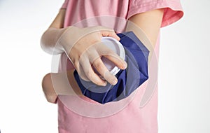 A girl in a pink T-shirt applies an ice bag to her elbow joint for an elbow injury. Local cryotherapy. Pain relief with