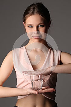 Girl in pink top holding glass of water. Close up. Gray background