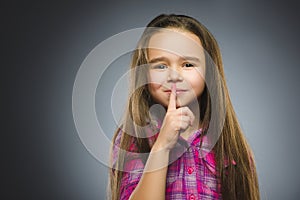Girl placing finger on lips asking shh, quiet, silence on gray background