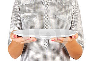 Girl in the plaid shirt is holding an empty round white plate in front of her. woman hand hold empty dish for you desing. perspect