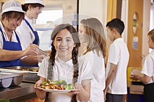 Girl with plaits holding plate of food in school cafeteria photo