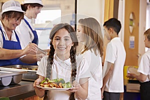 Girl with plaits holding plate of food in school cafeteria