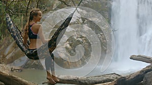Girl with Plaits Sits on Hammock against Waterfall