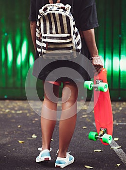 Girl with plastic orange penny shortboard behind green wall in cap photo