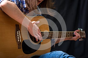 Girl playing an acoustic guitar on a dark background in the Studio. Concert young musicians