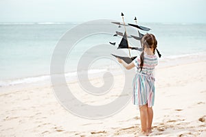 Girl playing on beach flying ship kite. Child enjoying summer.