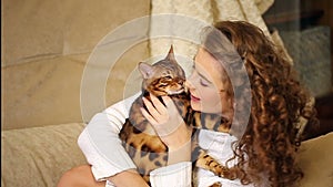 Girl playing and biting Bengal cat.