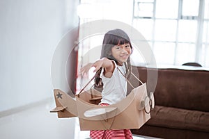 girl playing with cardboard toy airplane at home