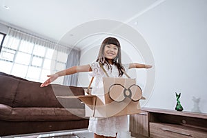 girl playing with cardboard toy airplane at home