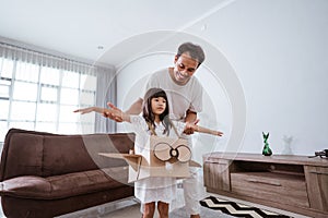 girl playing with cardboard toy airplane at home with father