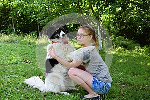 Girl playing with dog on grass. Teenager hugging Carpathian Shepherd Dog in the summer park. Friendship concept of man and animal