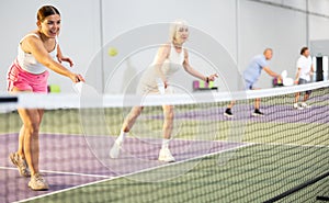 Girl playing doubles pickleball in team with older woman indoors