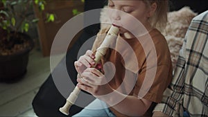 Girl playing the flute sitting next to her mother on the couch