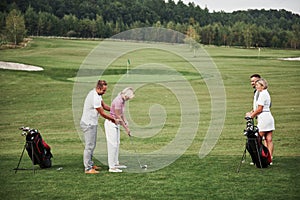 Girl playing golf and hitting by putter on green. Her teacher helps to explore the technique and make her first strikes