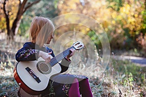 Girl playing guitar in the autumn forest