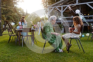Girl playing on guitar for her grandmother at garden party. Love and closeness between grandparent and grandchild.
