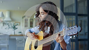 Girl playing guitar in living room. Musician playing chords on string instrument