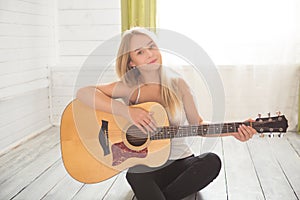 Girl playing guitar and singing. Young woman with long hair studying music at home. Woman sitting on floor and plays