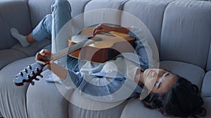 Girl playing guitar on sofa. Relaxed musician playing chords on acoustic guitar