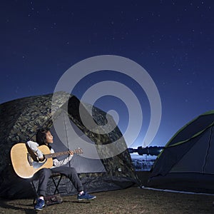 Girl playing guitar at tent glows under a night sky