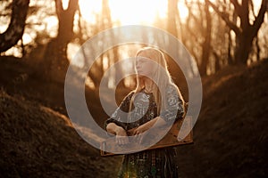 Girl playing the harp at sunset in the forest