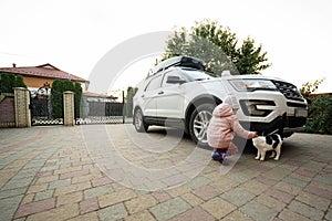 Girl playing with his cat in the yard of house, near family car