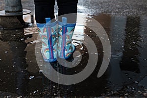 Girl playing jumping water puddles with rainbow blue boots on a urban scene