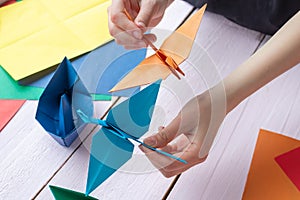 A girl is playing with an origami crane made of paper that she made herself. On a wooden background