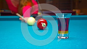 Girl playing pool, has the ball and is reflected in the glass