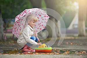 A girl playing in the puddle with the boat after rain