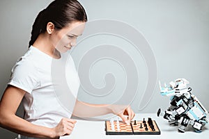 A girl is playing with a robot in chess. The robot sits opposite her on the table.