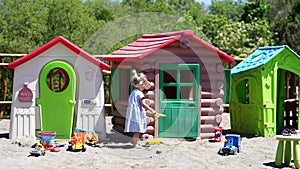 A girl is playing in the sand in front of a row of playhouses