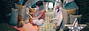 Girl playing with teddies in a tent made of bed sheets and chair