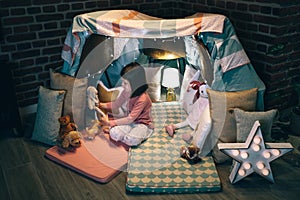 Girl playing with teddies in a tent made of bed sheets and chairs