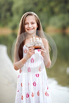 Girl playing with a toy sailing ship by the river