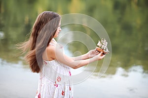 Girl playing with a toy sailing ship by the river