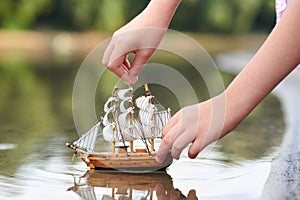 Girl playing with a toy sailing ship by the river