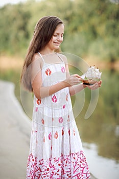 Girl playing with a toy sailing ship by the river