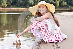 Girl playing with a toy sailing ship by the river