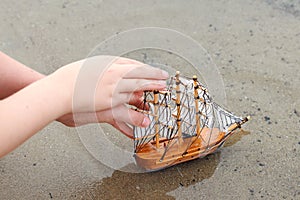 Girl playing with a toy sailing ship by the river, hand closeup