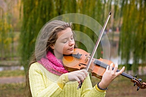 Girl playing the violin in the autumn park at a lake and willow foliage background