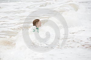 Girl playing in waves, having fun, dressed in protective wetsuit