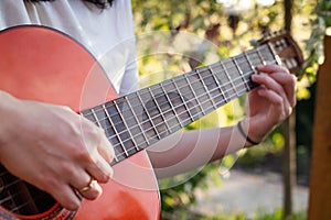 A girl plays an acoustic guitar in the garden. Close-up of female hands playing a classical guitar