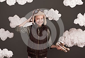 A girl plays with a cardboard airplane and dreams of becoming a pilot, dressed in a retro style jacket and helmet with glasses,