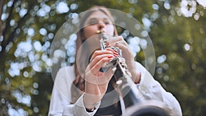 A girl plays the clarinet in the park in the summer.